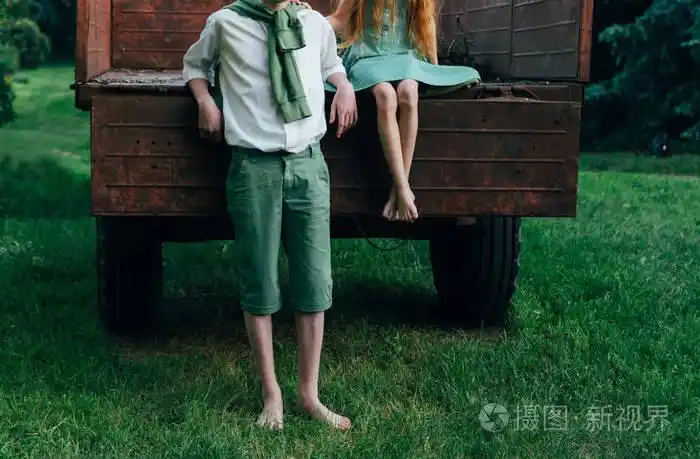 一个穿着绿色连衣裙的赤脚女孩坐在一辆旧大篷车里, 在她身旁, 赤脚
