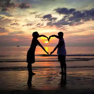 年轻夫妇心形海沙滩上在日落时手牵手