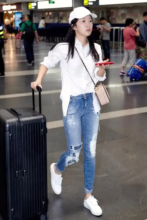 李念独自现身机场,头戴棒球帽,身穿白色不规则休闲衬衫,牛仔裤,脚踩