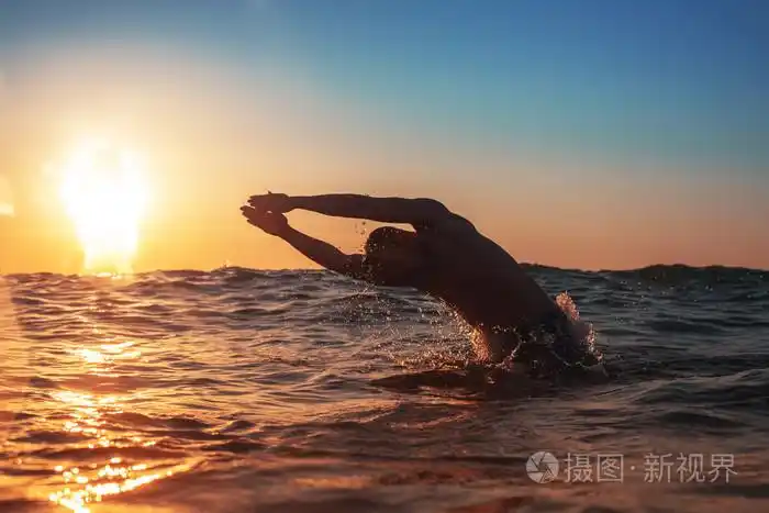 年轻人在黄色的日出在海里游泳