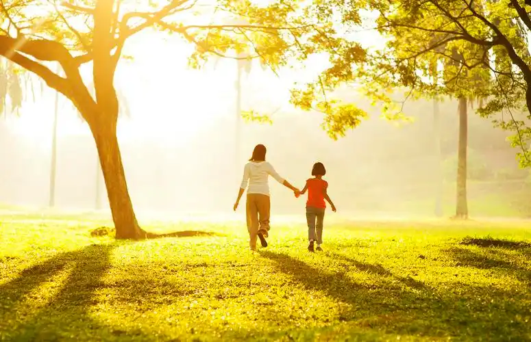 母亲牵着女儿的手在大树下