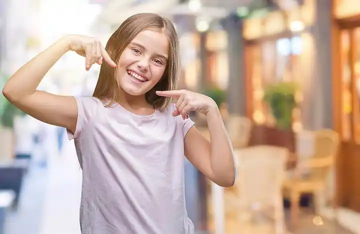 年轻美丽的女孩在孤立的背景下微笑着自信地显示和指着手指的牙齿和