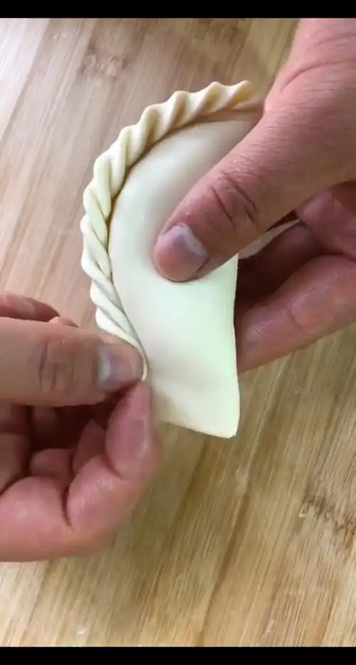左手推褶2挤饺子中间对折捏上,把饺子架在户口上,向中间挤3花边饺子