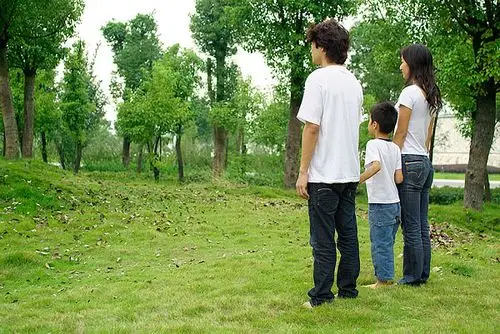 树林里手牵手站着的三口之家的后视图