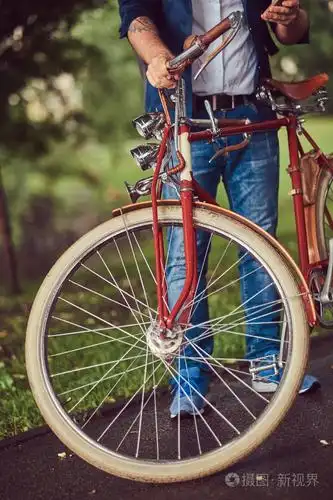 旅行者穿着休闲服装与背包使用智能手机放松在一个城市公园后骑着复古