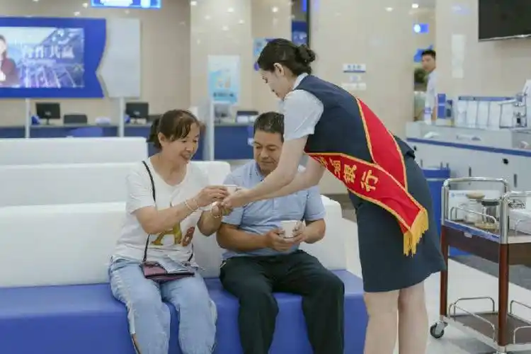 图为天山农商银行天山区支行大堂经理为等候办理业务的客户递上热水