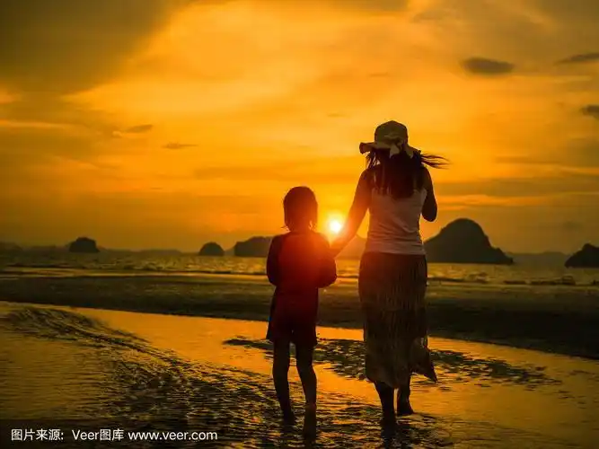 母亲节快乐,家庭活动理念.日落时分,妈妈牵着孩子在海滩上散步的剪影.