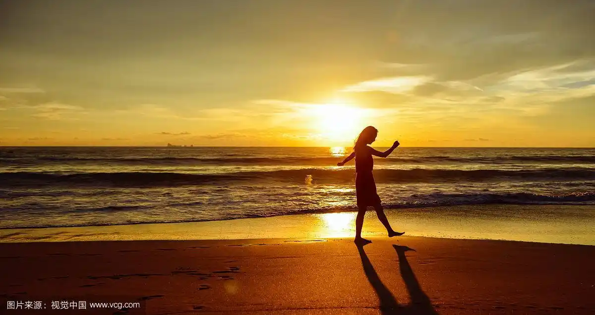 日落时分,一个女人沿着海滩散步的剪影