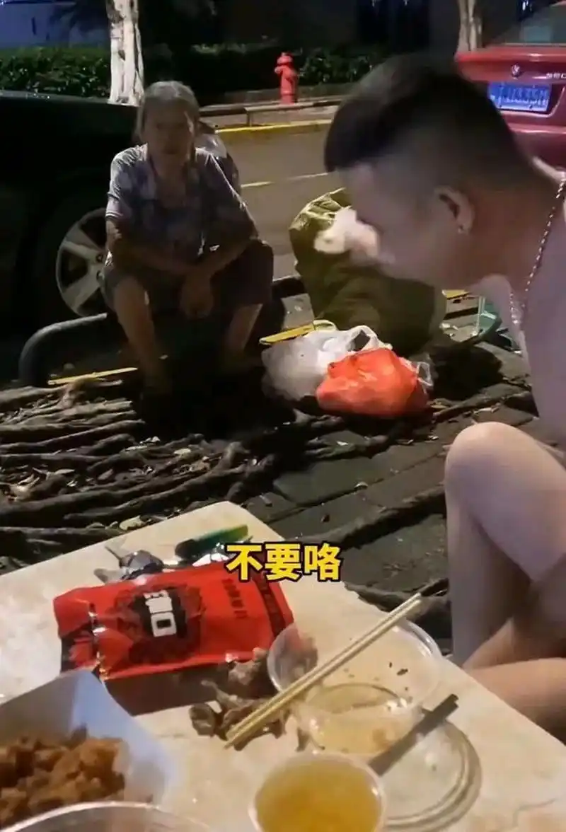 广东,一个赤裸着上身的男人和朋友在马路边饮酒,一位捡垃圾的大妈"不