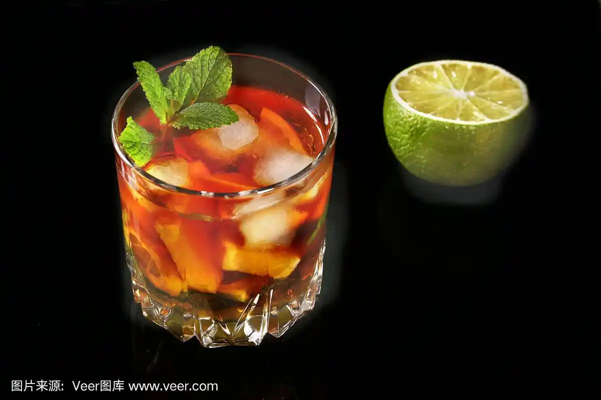一杯黑朗姆酒鸡尾酒,在黑色镜面背景上加入青柠,橙,冰块和薄荷叶.