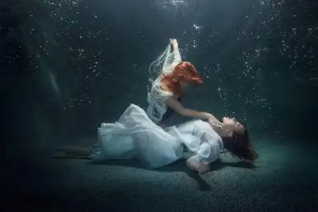 年轻女子躺在水底下, 另一位妇女牵着她的手靠在脖子上.照片