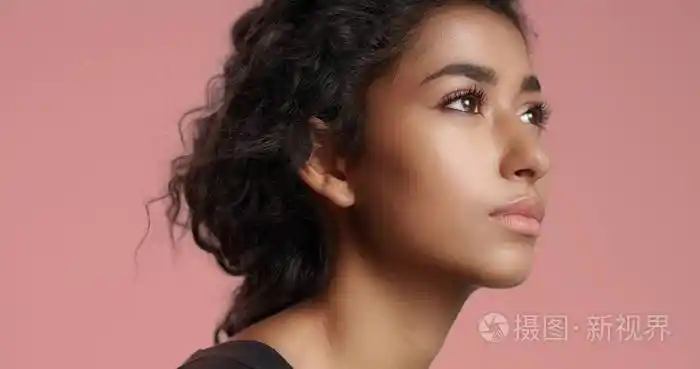 年轻女孩与完美浅褐色的皮肤和乌黑卷曲的头发美丽对着镜头微笑