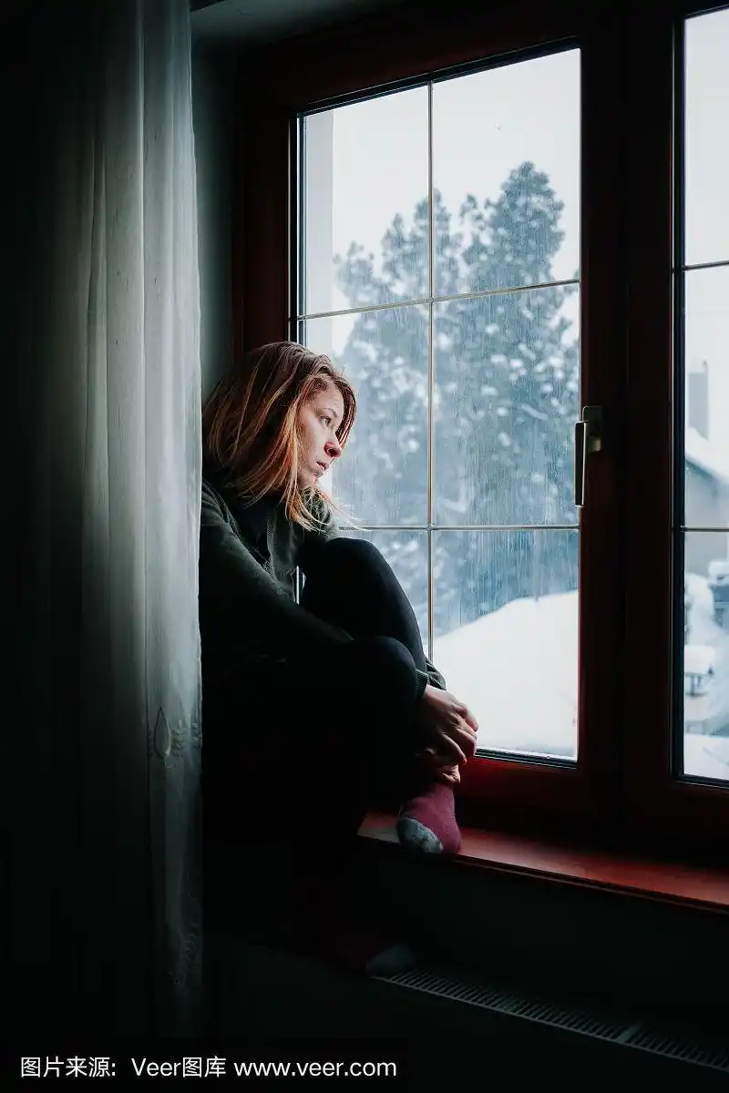 悲伤的女人坐在窗边望着外面