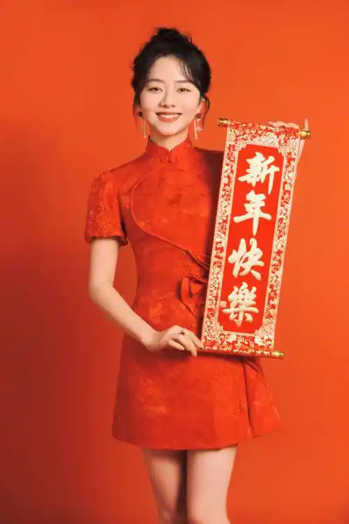 画面中的谭松韵身穿大红色的旗袍款连衣裙,手中拿着写有"新年快乐"的