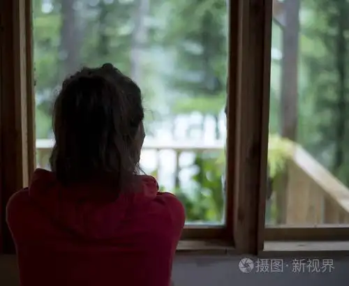 年轻的棕色头发女性看窗外的房子在森林下雨天