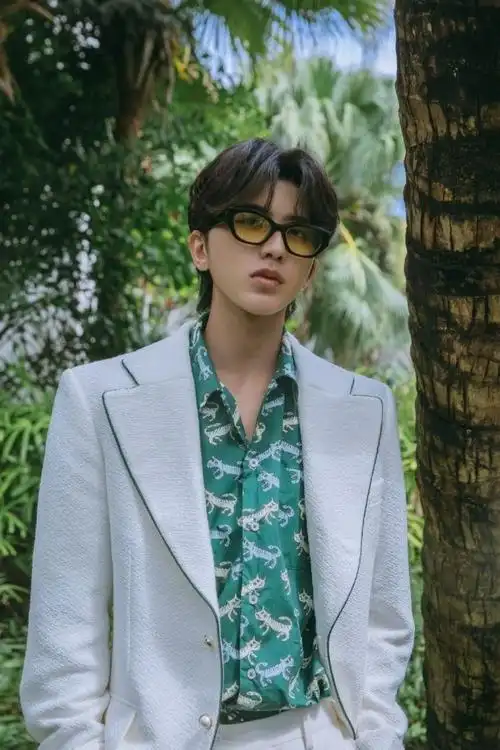 蔡徐坤身着全套白色西装,内搭绿色虎纹花衬衫,佩戴黑框墨镜,绅士又不