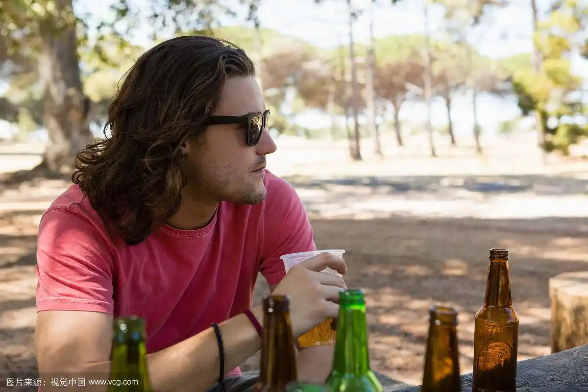戴墨镜的年轻人在公园喝啤酒