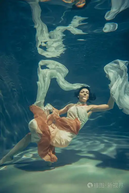 优雅苗条的女孩在水下游泳,就像一个自由潜水员穿着白色的晚礼服和