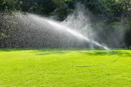 水在绿色的草地上在炎热的夏日, 草坪洒水喷头在花园的草地上喷洒水