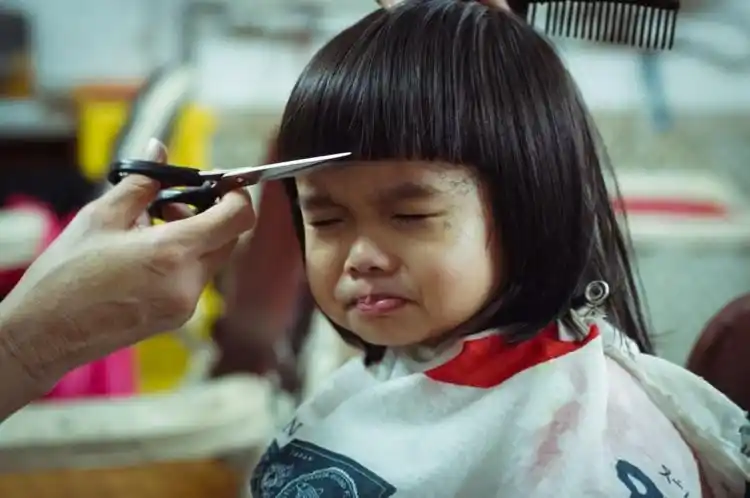 在理发店,沾满碎发的小女孩没有哭闹,只是表情有点苦苦闷闷.