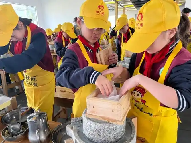 在研学基地老师们的指导下,孩子们将泡好的黄豆少量多次地加入到石磨