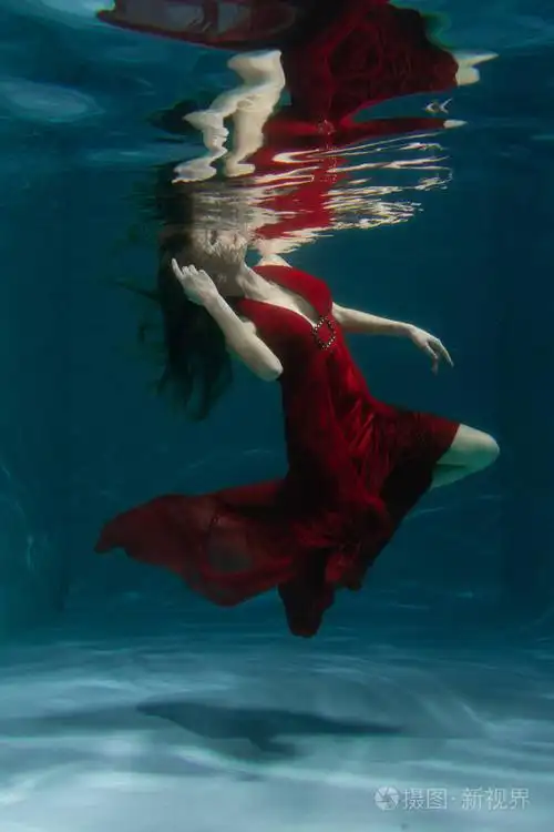 一个美丽的自由潜水员,一个人穿着红色的长裙,独自在深水中游泳