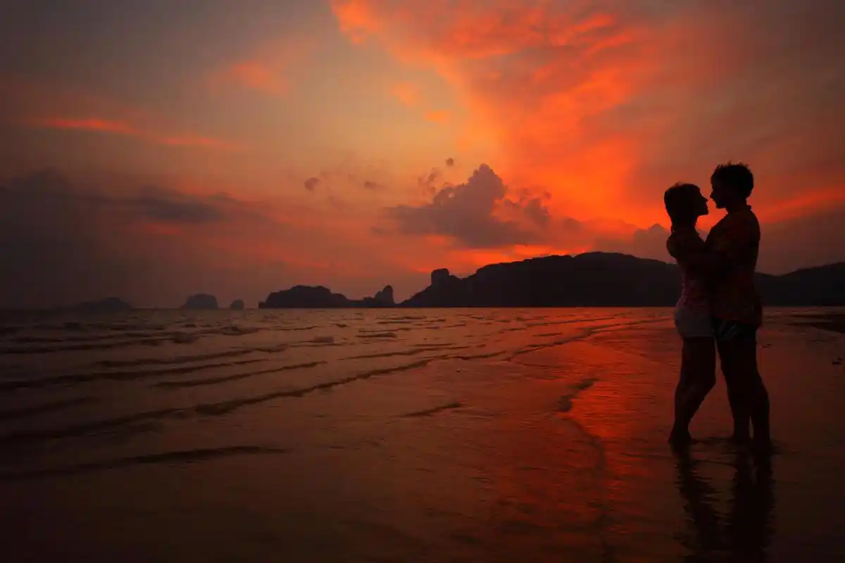 两个年轻的恋人站在湿海滩上和日落背景上拥抱幸福情侣图片