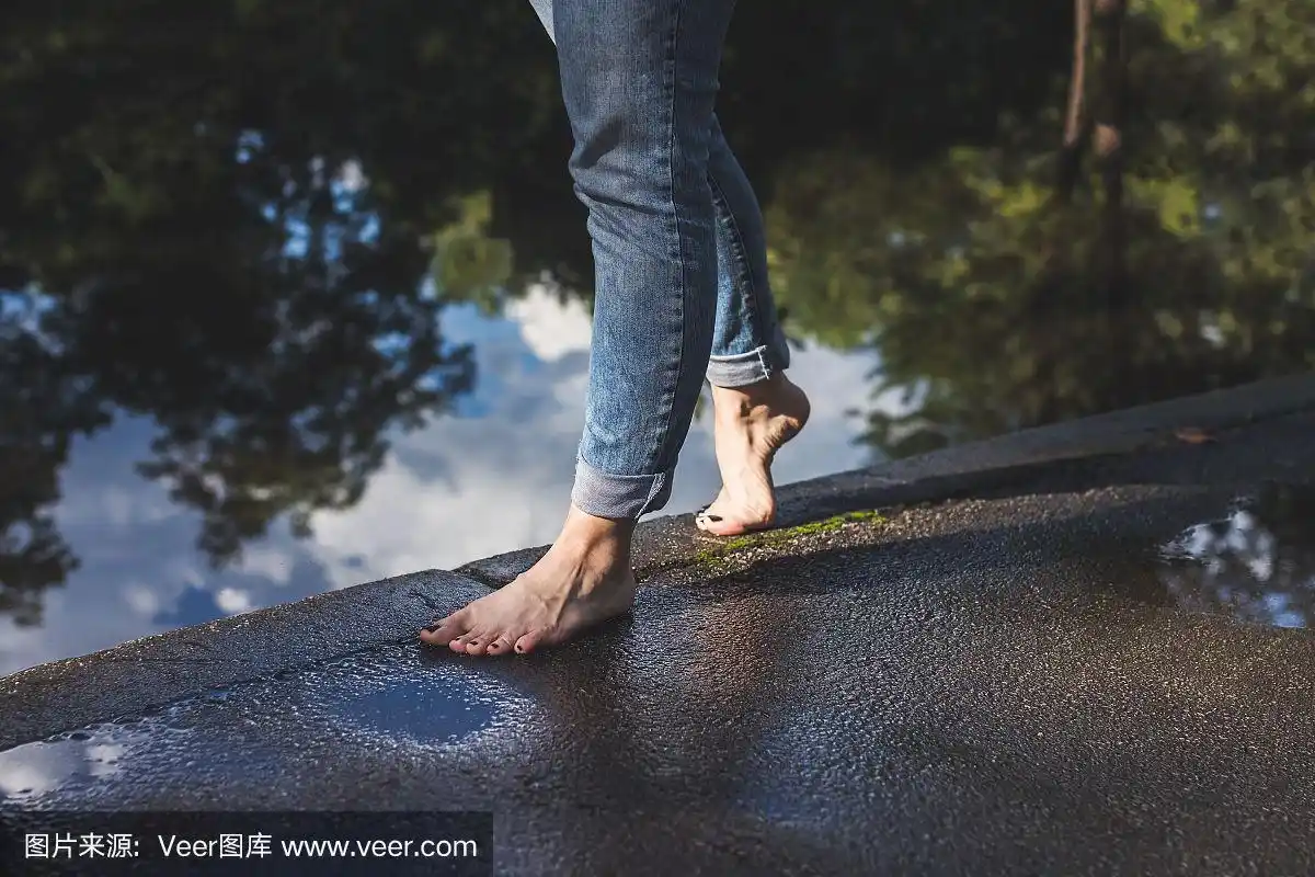 穿着蓝色牛仔裤的赤脚女人走在水边