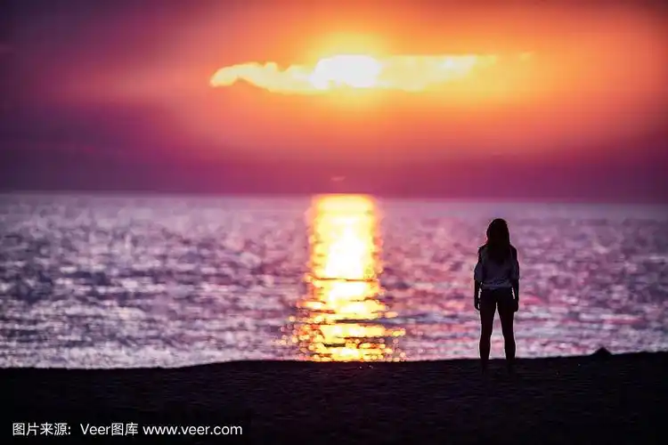 一个女人从海滩看日落的背影.