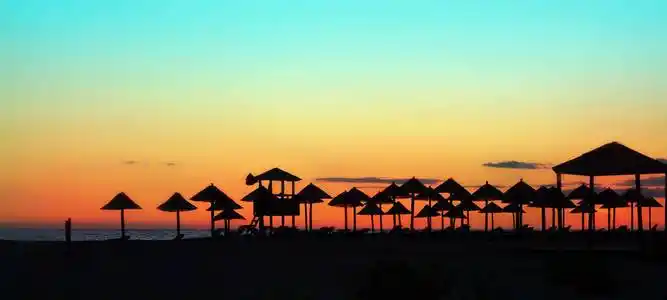 横向的全景俯瞰大海日落和海滩遮阳伞站在水边的剪影照片