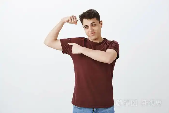 t恤衫的英俊阳刚的男人的肖像, 举手和显示肌肉, 用食指指着手臂, 在