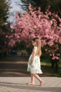 快乐的女孩儿赤脚走在公园里,背景是粉红色的樱花树.检疫结束.