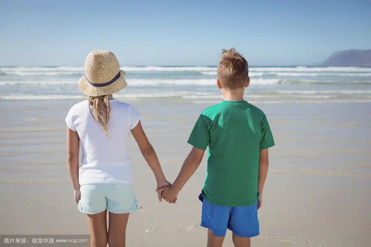 在阳光明媚的日子里,兄弟姐妹手牵手在海滩上的后视图