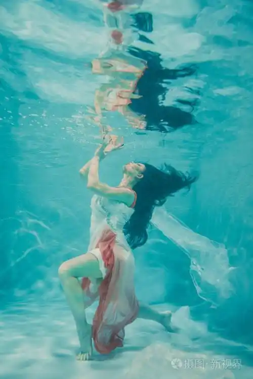 美丽的模特儿在水下游泳,穿着女性的白色和粉红色长裙