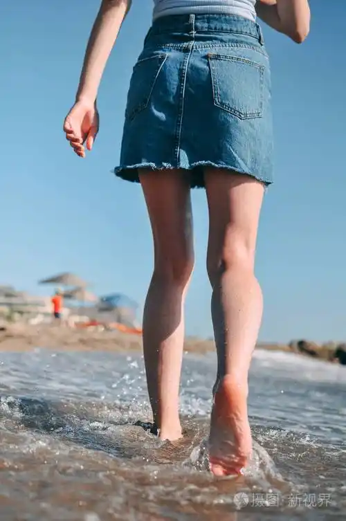 一个年轻的女孩赤脚跑在海边沙滩上从后面的底部视图