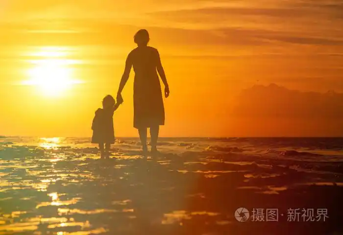 母亲和小女儿在日落时在海滩上行走