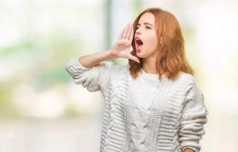 年轻美丽的女人在与世隔绝的背景下穿着冬天的毛衣喊着大声尖叫到一边