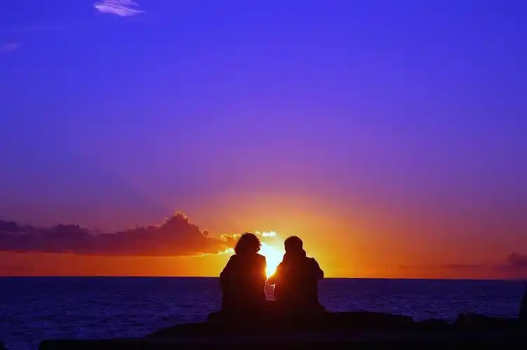 浪漫梦幻紫色风景夕阳下海边岩石上的恋人情侣两个人剪影幸福情侣七夕