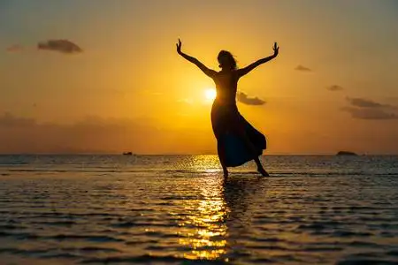 夕阳下,在天堂岛的热带海滩上跳舞的年轻美女.夏季概念.假日旅行.照片