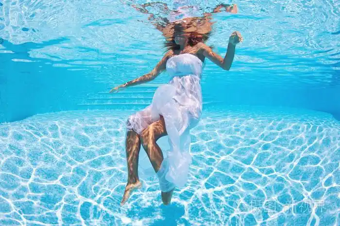 在游泳池中的白色礼服的水下女人时尚人像