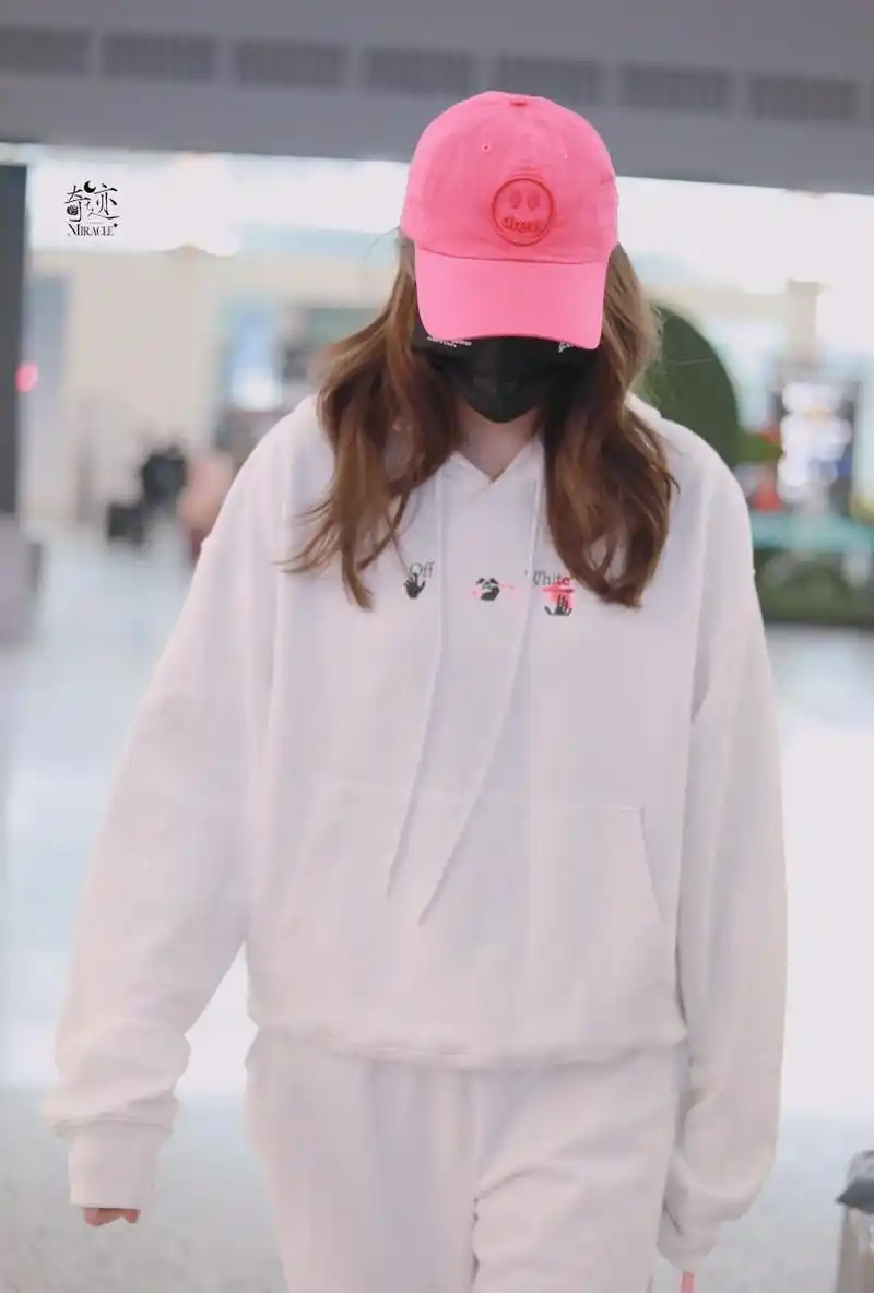 关晓彤机场私服穿搭,白色印花连帽卫衣搭配白色运动裤,粉色鸭舌帽搭配