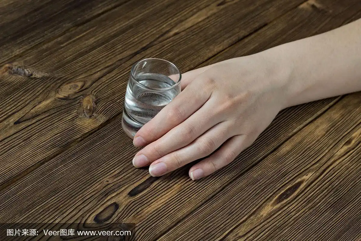 女人的手拿着一杯酒放在木桌上,特写