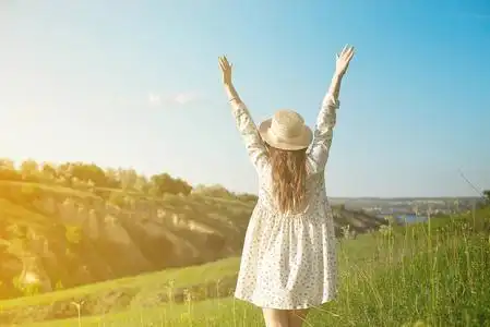 日本在夏天的阳光下一个快乐的女人,戴着草帽,张开双臂,在夕阳的照耀