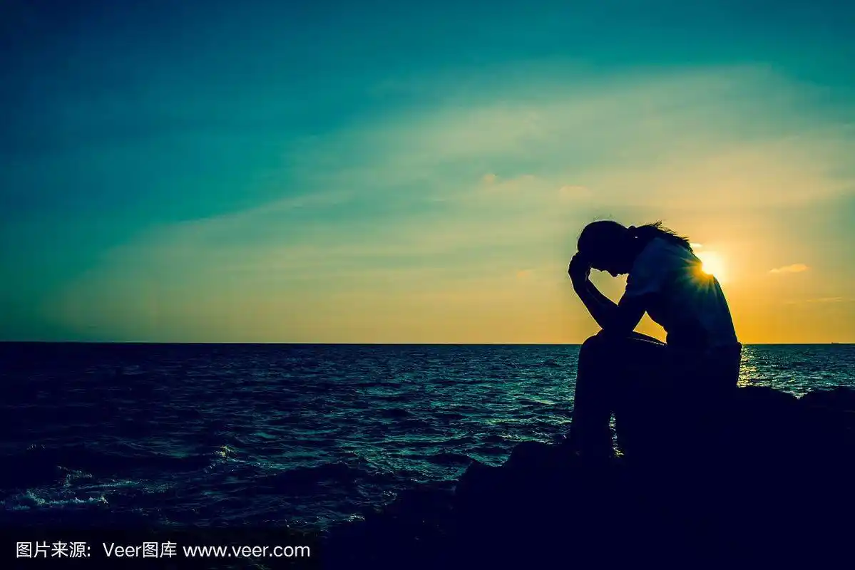 女人独自坐在岩石上的剪影.悲伤和孤独.