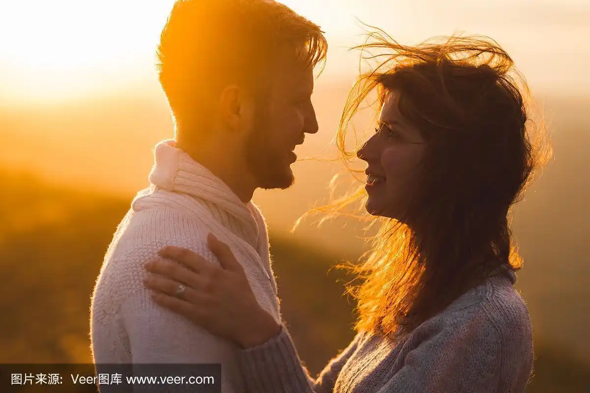 温柔的特写男女在一起,开心的看着对方.剪影在美丽的夕阳下,风在发