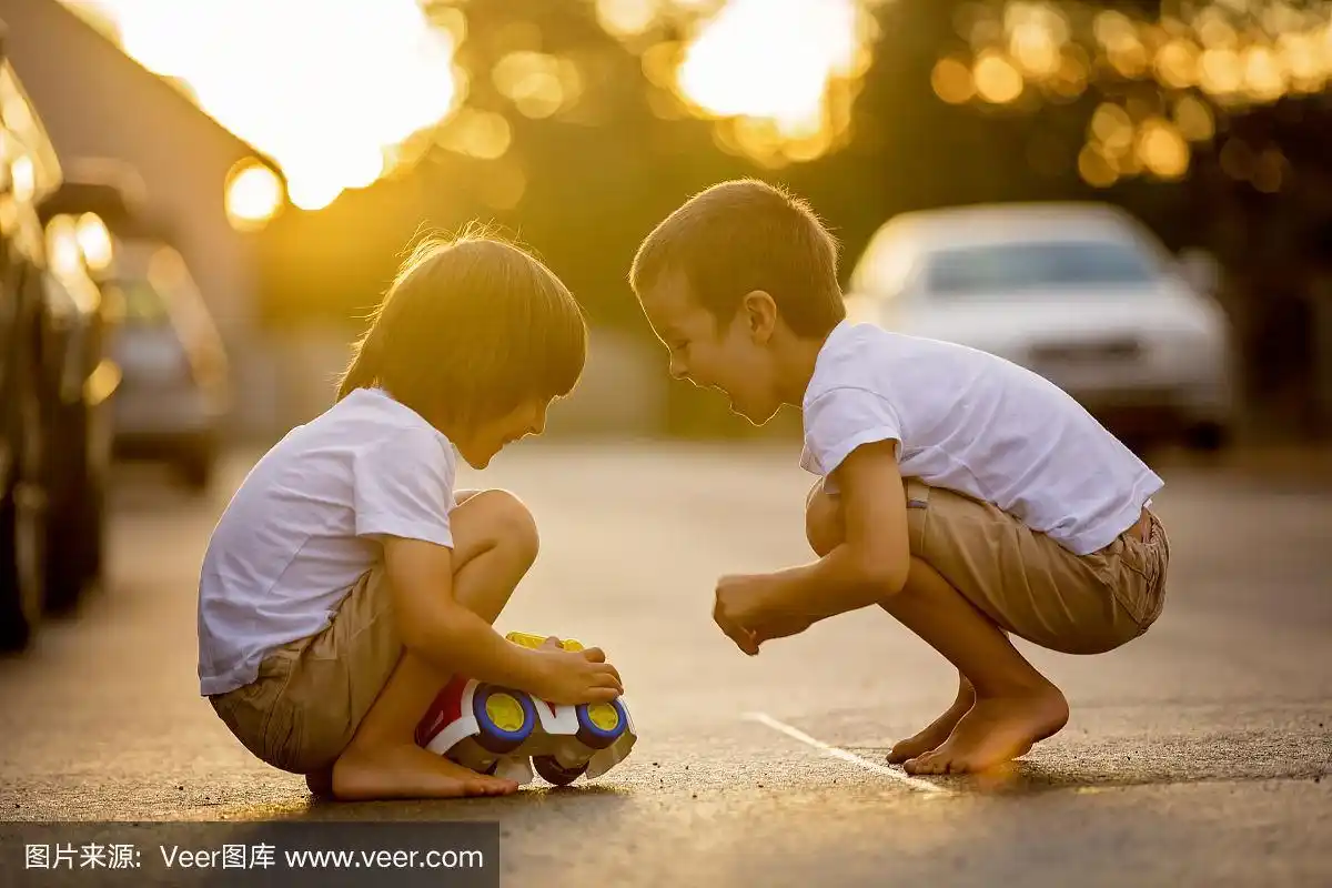 两个可爱的孩子,男孩兄弟,在乡村的街道上玩汽车玩具,在日落,夏天的