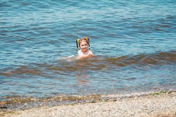 夏天,穿着泳衣的小女孩在海里洗澡,溅起水花,在水中奔跑照片-正版商用