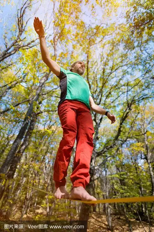 广角男走钢丝者平衡赤脚在松驰线在秋天的森林.