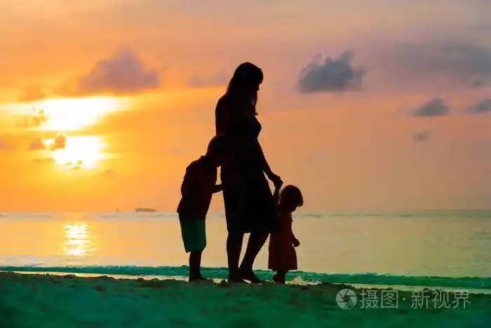 母亲和两个孩子在日落时在海滩上行走