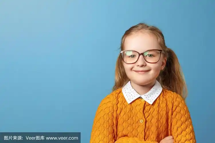 小女孩戴眼镜的近距离肖像.蓝色背景下穿着黄色毛衣的漂亮孩子.本空间